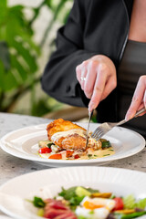 A close-up of a person cutting into a delicious, crispy chicken dish served with fresh vegetables. The vibrant colors of the salad in the background enhance the appealing presentation.