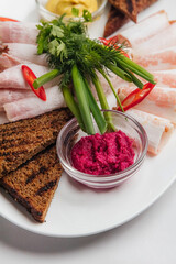 Thinly sliced ukrainian salo served with mustard, horseradish, rye bread, green onions, dill and red chili peppers arranged on white oval plate. Restaurant or cafe menu, cookbook recipe