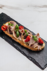 Elegant crostini topped with thinly sliced roast beef, fresh basil leaves, and sun-dried tomatoes, served on a black slate plate. Restaurant or cafe menu, cookbook recipe