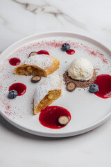Apple strudel with powdered sugar, accompany a scoop of vanilla ice cream, drizzled with berry coulis and topped with fresh blueberries and chocolate shavings. Restaurant or cafe menu, cookbook recipe