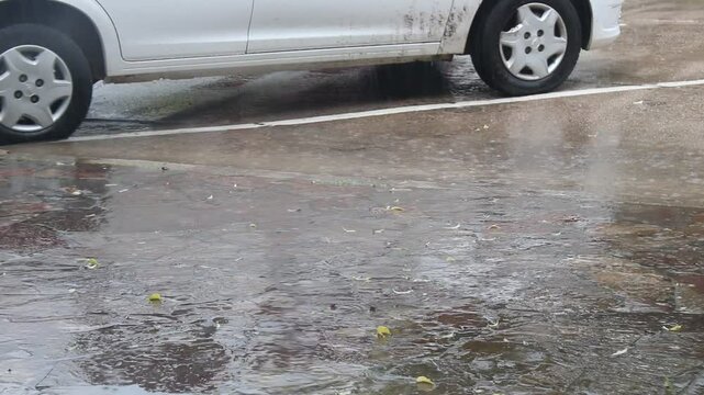 Cae la lluvia sobre la calle de asfalto,  formando c&iacute;rculos y corrientes de agua mojando el auto aparcado en el estacionamiento.