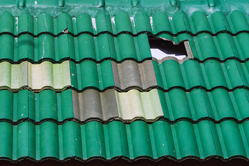 Fototapeta premium Broken monier green tiles roof. Fallen shingles on house. Large hole in old tiled roof. Missing and slipped plain clay roof tiles on pitched roof. Hole created by missing tile on dilapidated old roof