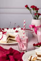 milkshake with red berries of currants, raspberries, cherries in tall glasses with red straws, in the background a heart-shaped tiramisu cake, red flowers in a vase, mousse cake, Valentine's Day