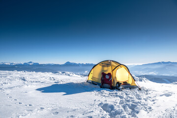 Yellow camp tent with an open zipper on deep white snow, against the sunlight in the mountains. © XArt