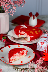 heart-shaped mousse cake in red glaze with gold decor on a white plate, red and pink carnations, roses, gypsophila in a vase, Valentine's Day cake, birthday, light background, food photo