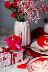 red candle in a glass candlestick, red and pink carnations, roses, gypsophila in a vase, Valentine's Day cake, birthday, light background, holiday decor