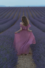 Ein M&auml;dchen mit offenen Haaren in einem wehenden Kleid in einem Lavendelfeld am Abend.