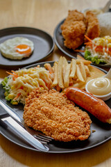 Fried fish steak with sausage dressing, rice and rosemary on black plate on wooden table.