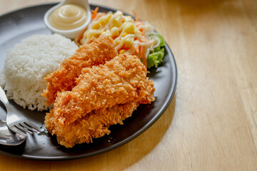 Fried fish steak with sausage dressing, rice and rosemary on black plate on wooden table.