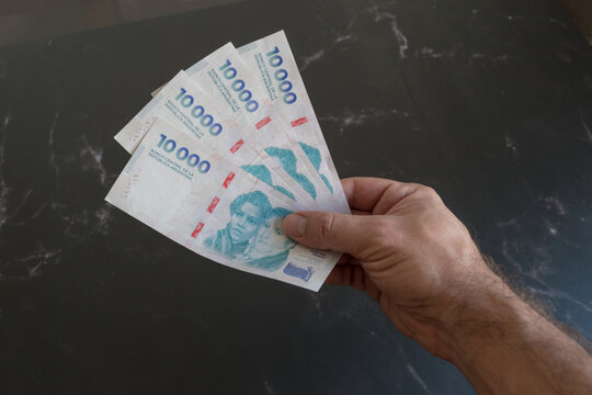 billetes de 10 mil pesos argentinos sostenidos por la mano de un hombre latino.