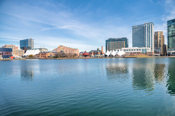 Baltimore's Inner Harbor with Skyscrapers under a blue sky reflected in the water.