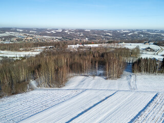 Obraz premium Aerial view of a snowy landscape with rural fields and sparse trees under a clear blue sky, creating a serene winter atmosphere.