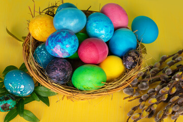 Colorful easter eggs in a basket on a yellow wooden table
