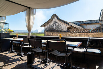 A serene outdoor café with a stunning countryside view, featuring a table set with a glass bottle of lemon water, a drinking glass, and a small flower vase. 