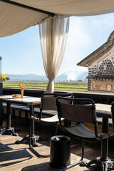 A serene outdoor café with a stunning countryside view, featuring a table set with a glass bottle of lemon water, a drinking glass, and a small flower vase. 