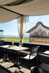 A serene outdoor café with a stunning countryside view, featuring a table set with a glass bottle of lemon water, a drinking glass, and a small flower vase. 