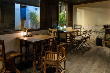 A cozy and atmospheric café at night, featuring rustic wooden tables and chairs illuminated by warm lantern light. The setting exudes a vintage charm with wooden window frames, textured walls, 
