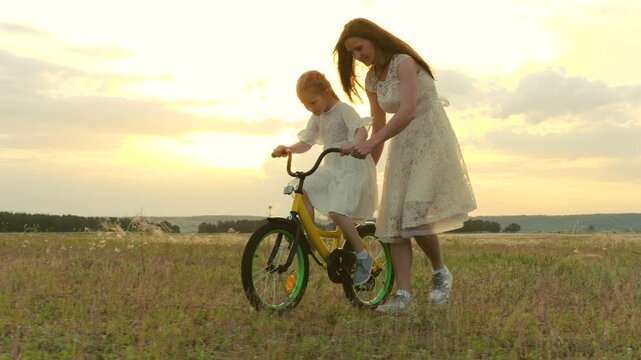 happy family. child girl learning ride bike. mom daughter kid spend time bike park. concept children dream. mother child play outdoors. little girl pedals steers bicycle park. young mother with kid
