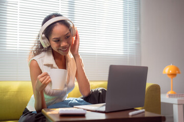 Happy young woman working remotely from home sitting on a comfortable sofa, enjoying a cup of...