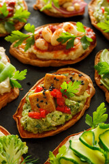 Sweet potato toasts with various vegetarian toppings, focus on the  toast with  avocado paste and baked tofu in the middle, close-up view.