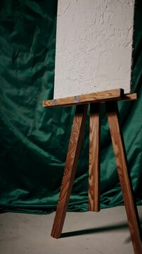 A vintage wooden easel holding a textured blank canvas against a rich green artistic backdrop.