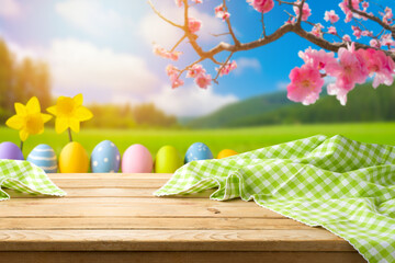 Easter holiday concept with empty wooden table, tablecloth and easter eggs over spring  flower blossom and green meadow background