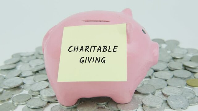 Charitable Giving text on a yellow note with a hand inserting coins into a piggy bank, symbolizing donations and generosity