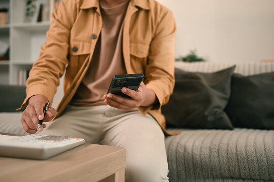 Budgeting and financial tracking made easy at home, close-up shot of a man using a calculator and a smartphone