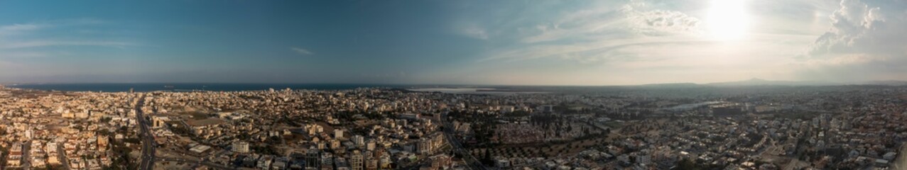 Aerial panoramic view of a sprawling cityscape under a partly cloudy sky.