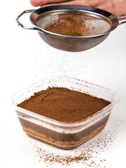 A hand sifts cocoa powder onto a rich chocolate pudding cake dessert, showcasing a layering of flavors in a home kitchen environment