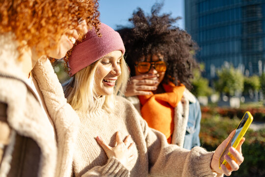 Three women sharing a joyful moment while looking at a smartphone.
