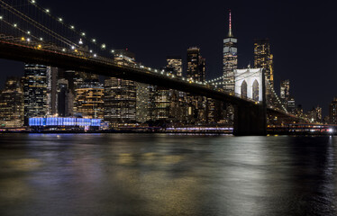 Obraz premium downtown manhattan new york city skyline with brooklyn bridge in the foreground at night (east river long exposure in dark darkness) lights office buildings skyscrapers travel tourism destination usa