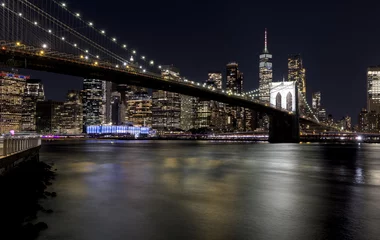 downtown manhattan new york city skyline with brooklyn bridge in the foreground at night (east river long exposure in dark darkness) lights office buildings skyscrapers travel tourism destination usa