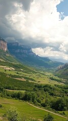 Fototapeta premium Mountain valley landscape with cloudy sky. Scenic view of a valley surrounded by mountains and fields. Possible use Nature stock photography