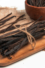 A bundle of aromatic vanilla beans tied with twine rests on a wooden board, accompanied by a rustic bowl filled with more beans