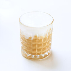 A creamy coffee drink is elegantly served in a textured glass, showcasing its smooth, frothy layer on top against a simple backdrop