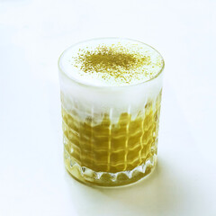 A vibrant green matcha beverage served in a textured glass, featuring a foamy top and a sprinkle of...