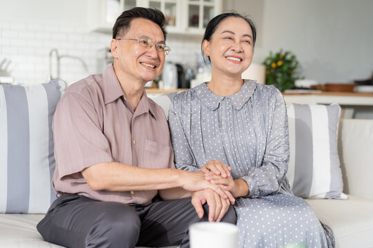 Happy Asian senior couple holding hands sitting on couch in the living room. Empathy and love with care of marriage people. Happy family lifestlye insurance