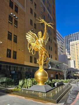 the gold Spirit of Communication statue at the AT and T Discovery District with office buildings,  lush green plants and a water fountain in downtown Dallas Texas USA