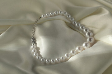 Beautiful pearl necklace on white silk, closeup