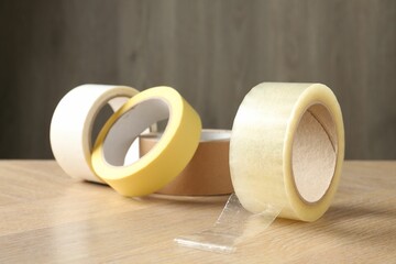 Rolls of different adhesive tapes on wooden table, closeup