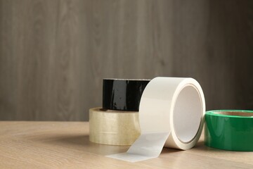 Rolls of different adhesive tapes on wooden table, space for text