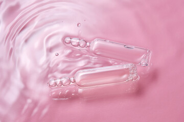 Ampoules in water on a pink background.
