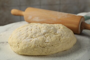 Fresh dough and rolling pin on table, closeup