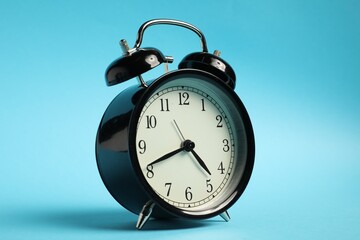 One black alarm clock on light blue background