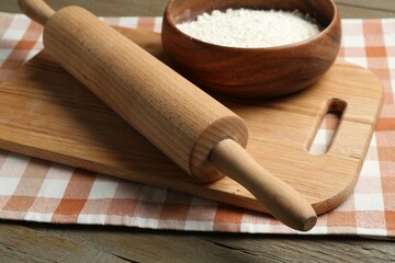 Rolling pin, bowl of flour and board on wooden table, closeup