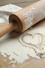 Rolling pin and heart shape made of flour on table, closeup