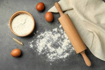 Rolling pin, bowl of flour, eggs and spike on grey table, flat lay