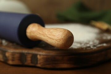 Rolling pin, wooden board and flour on table, closeup
