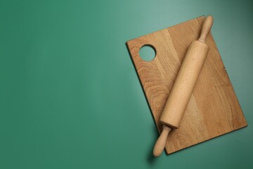 Rolling pin and wooden board on green background, top view. Space for text
